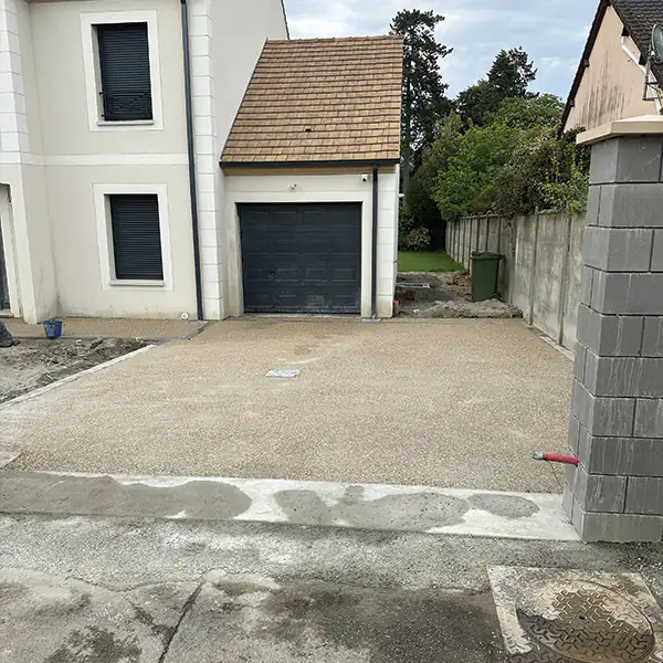 Cour gravillonnée et pilier en blocs béton près d'un garage