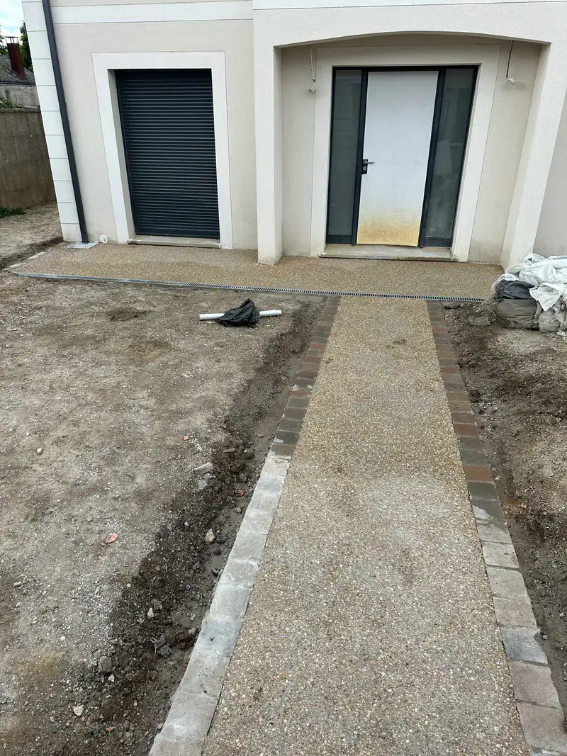 Allée en béton désactivé bordée de pavés devant une maison