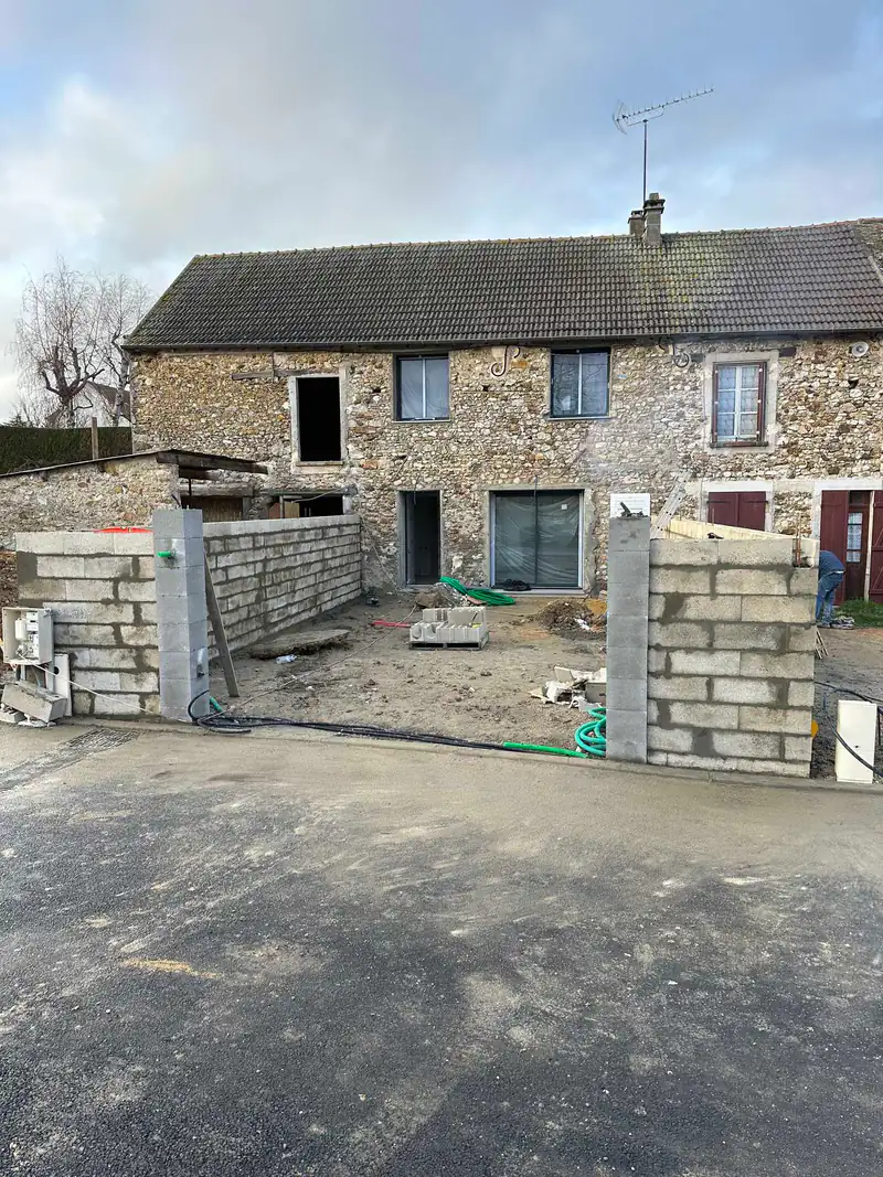 Chantier L&D Bâtiment : montage de murets en parpaings devant une maison en pierre