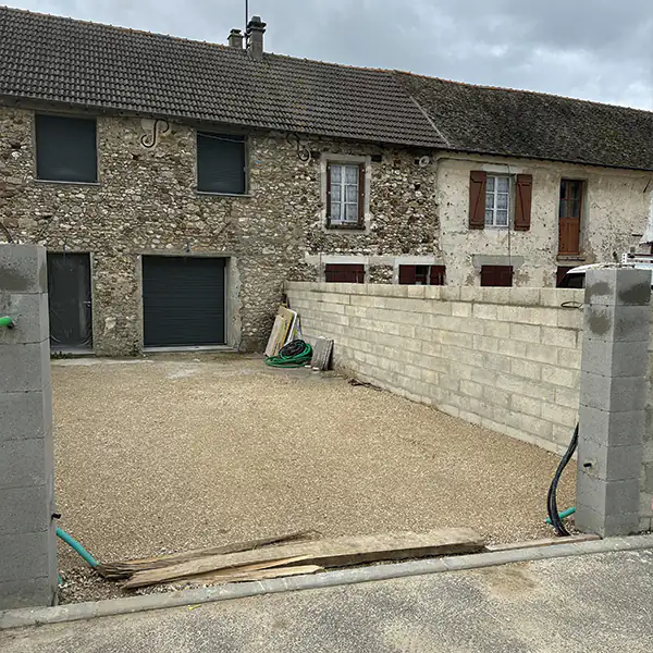 Cour avec murets et piliers en parpaings neufs devant une maison en pierre