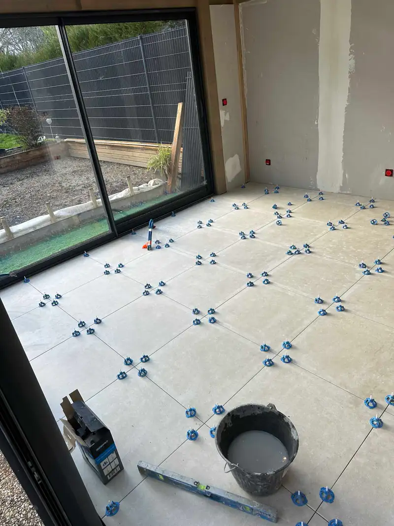 Carrelage grand format en cours de pose avec cales de nivellement